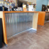 Stained and finished plywood reception and check out desks with metal base and inset corrugated metal panel.