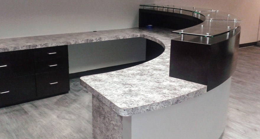Custom plastic laminate reception desk with plastic laminate cabinets, countertop and transaction top with glass-on standoffs.