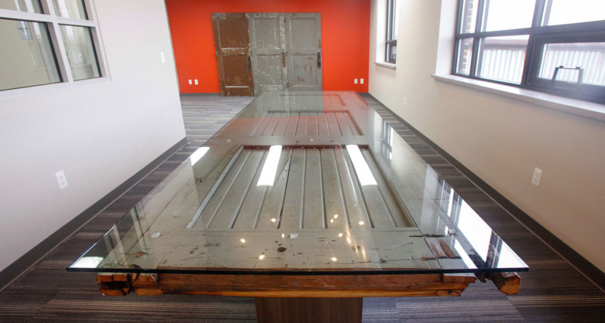 Reclaimed wood door re-purposed as a custom conference table with plastic laminate support bases and glass top.